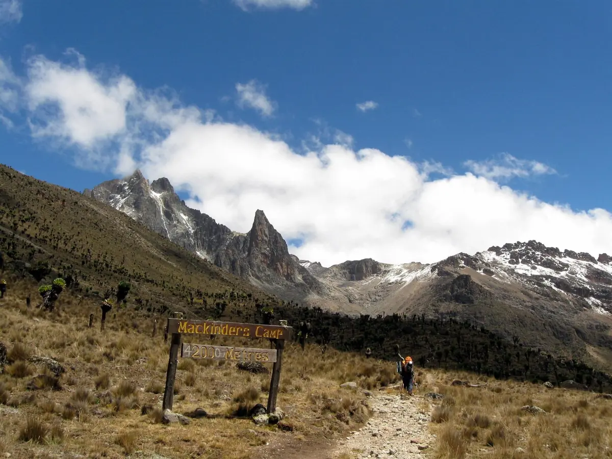 Trail with a signboard leads up a moorland valley toward snowy peaks