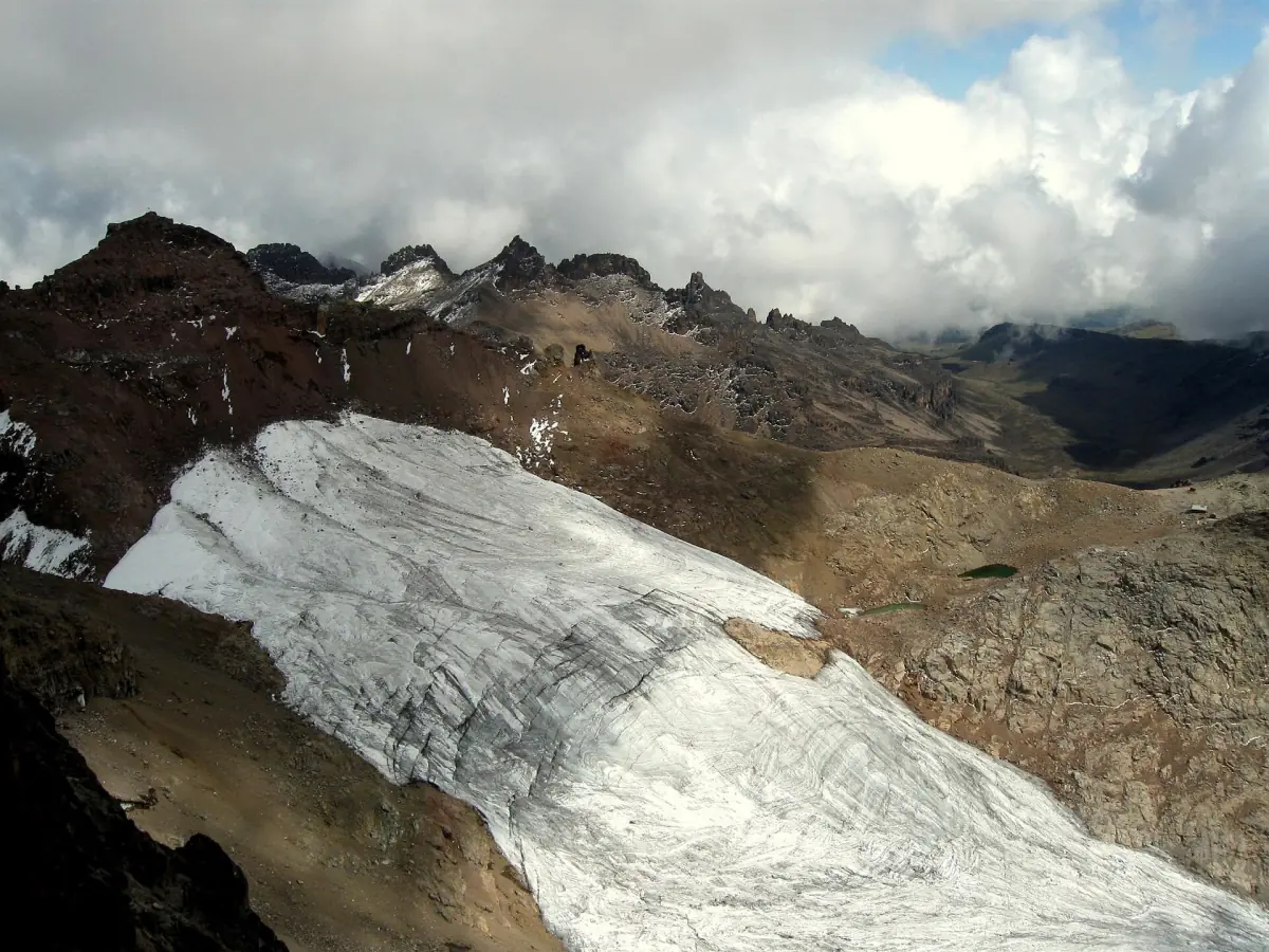 Sheet of glacier ice lies on dark rock below cloudy summits