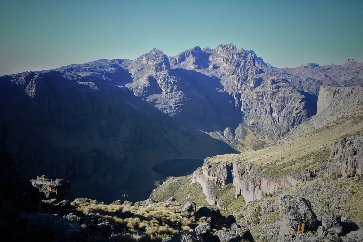 Dark lake lies between steep mountain ranges under a deep blue sky