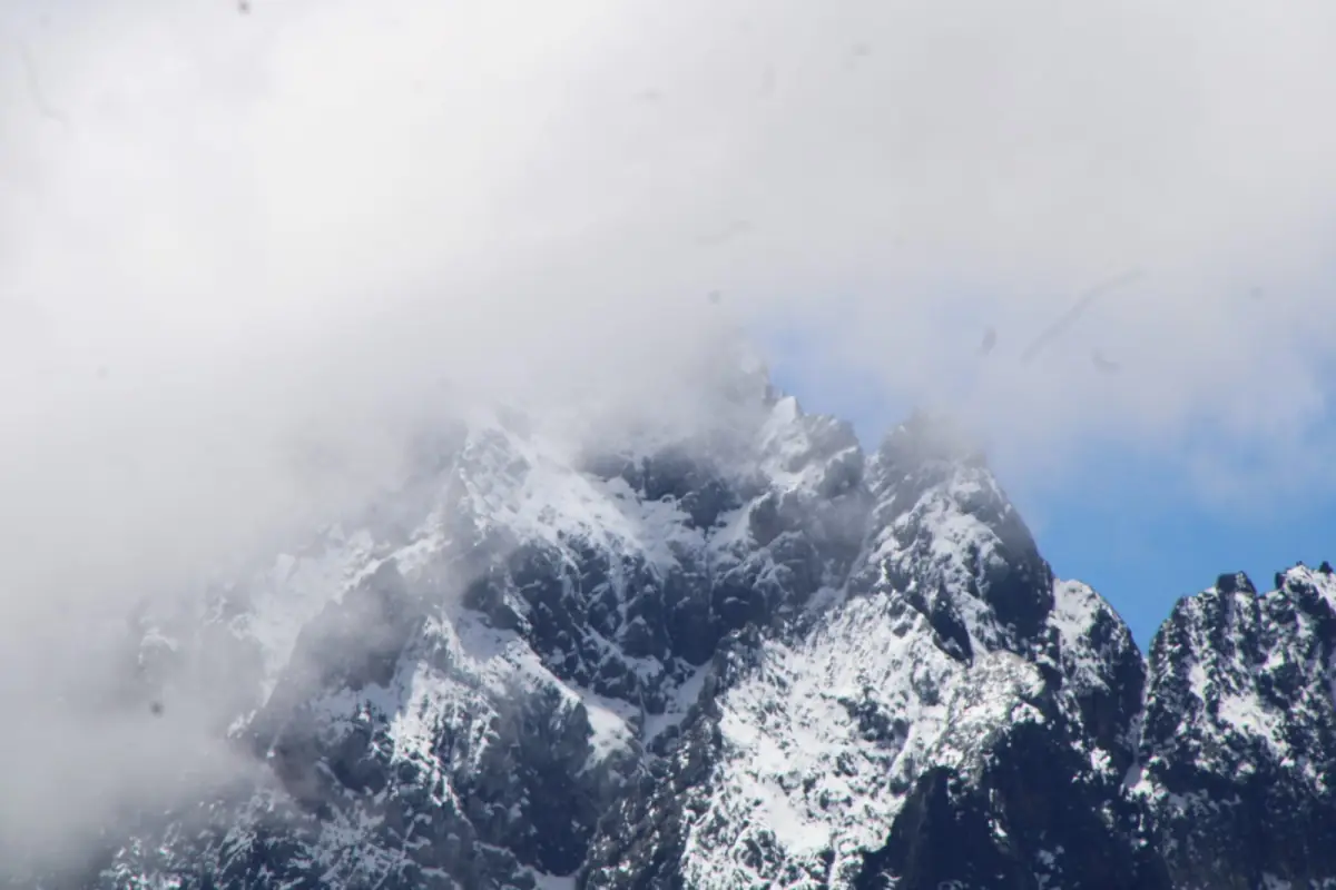 Snow-streaked rocky peaks emerge from thick drifting clouds