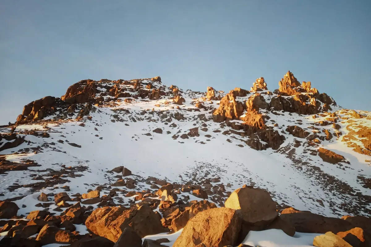 Snow-dusted orange rocks near the summit of Point Lenana in morning light