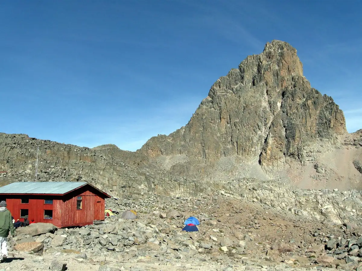 Un refuge de montagne rouge et une tente au pied d’un sommet rocheux escarpé